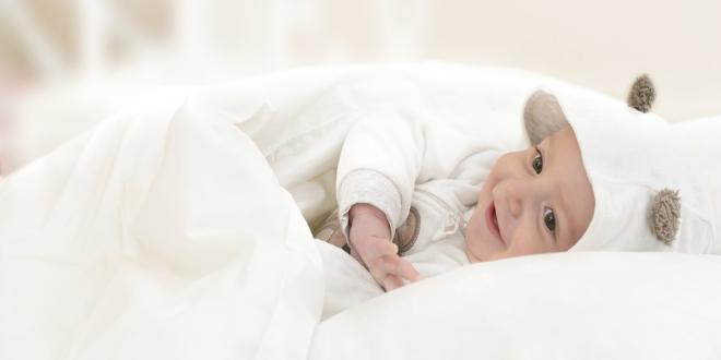 A happy baby smiling snuggled in a white blanket