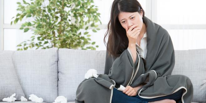 A woman on the couch with a blanket and a pile of tissues