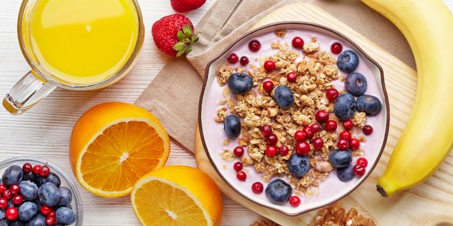 A bowl of granola, nuts, and yogurt with fresh fruits and juice