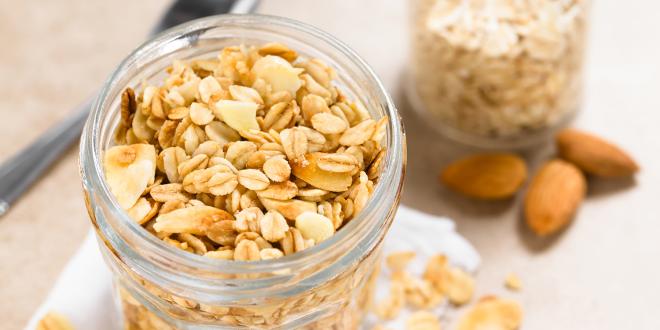 Coconut Almond granola in glass jar, ingredients and spoon in the background.